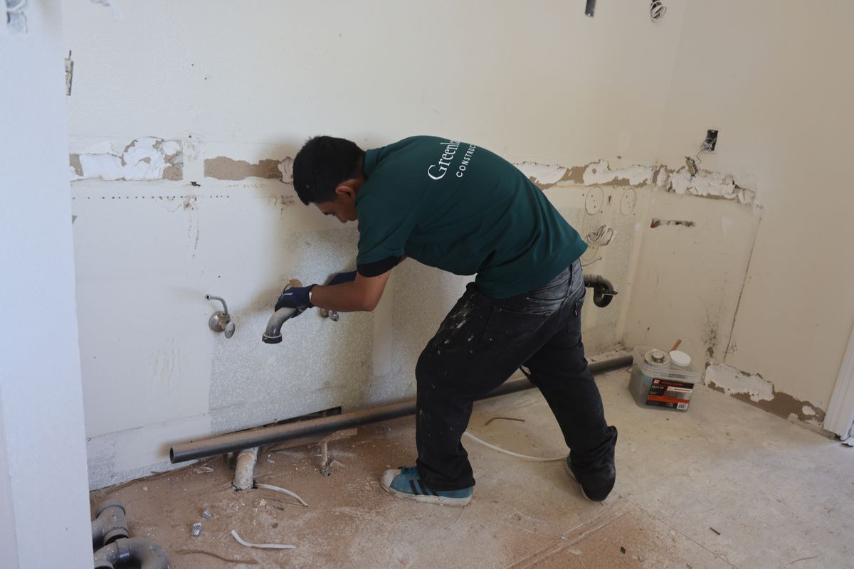 Greenland Construction crew member installing plumbing in a gutted room